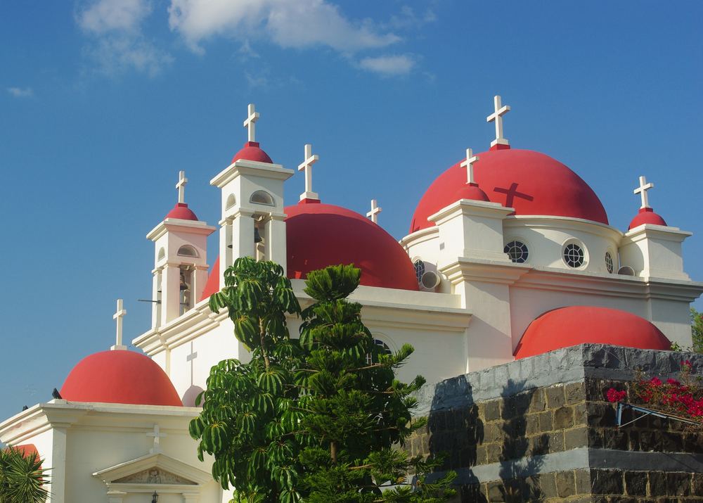 A white church with red domes standing beside Capernaum on the Sea of Galilee